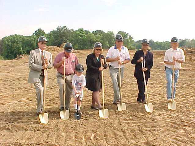 A group of people standing in the dirt with shovels.